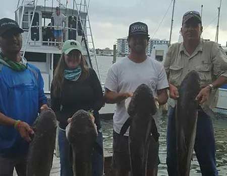 Anglers pose with their fish on a dock on a cloudy day. 